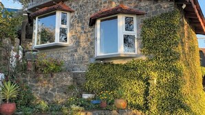 Una casa de piedra con balcón, un pequeño jardín y una escalera de piedra que lleva a la entrada.