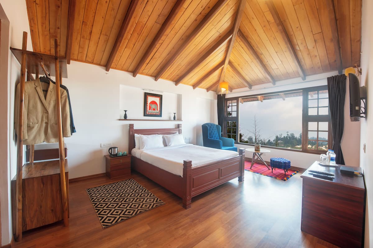 Une chambre avec un plafond en bois, un lit, une chaise, un bureau et une vue sur l’extérieur.