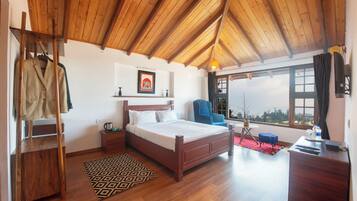 Un dormitorio con techo de madera, una cama, una silla, un escritorio y vistas al exterior.