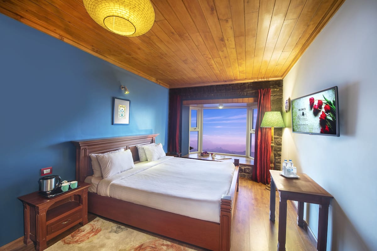 Une chambre d’hôtel avec un plafond en bois, un grand lit, une table de chevet avec une lampe, un téléviseur et une vue sur le coucher de soleil par la fenêtre.