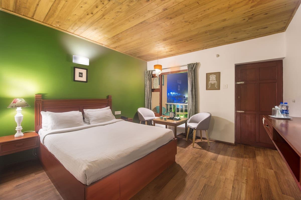 Une chambre d’hôtel avec un plafond en bois, un lit, un bureau avec une chaise, une table de chevet et une fenêtre avec des rideaux.