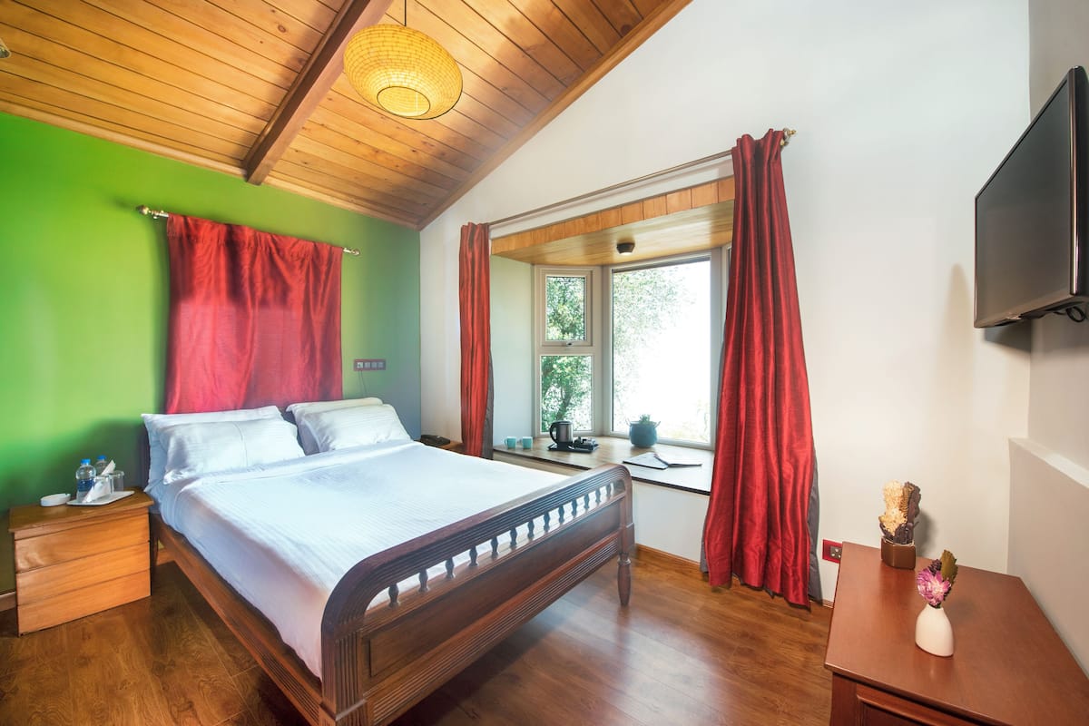 Une chambre à coucher avec un lit en bois, des murs verts, une fenêtre avec des rideaux, une table de chevet et un téléviseur à écran plat.