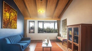 Una sala de estar con un sofá azul, una mesa de centro de madera, una estantería y un ventanal con vistas a árboles.
