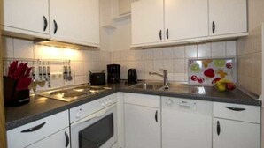 A kitchen with white cabinets, a stove, a sink, and a coffee maker. - Haus Nordstrand (Göhren)