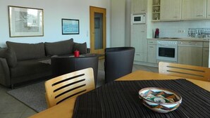 A compact living space with a sofa, a dining table, and a kitchen area. - Haus Nordstrand (Göhren)