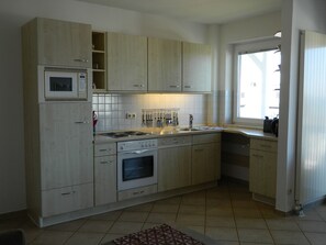 A kitchen with light wooden cabinets, a built-in microwave, a stove, and a sink. - Haus Nordstrand (Göhren)