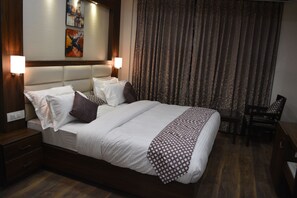 A hotel room with a large bed, two bedside tables, a chair, a desk, and a curtain. - Hotel Dolives (Panipat)