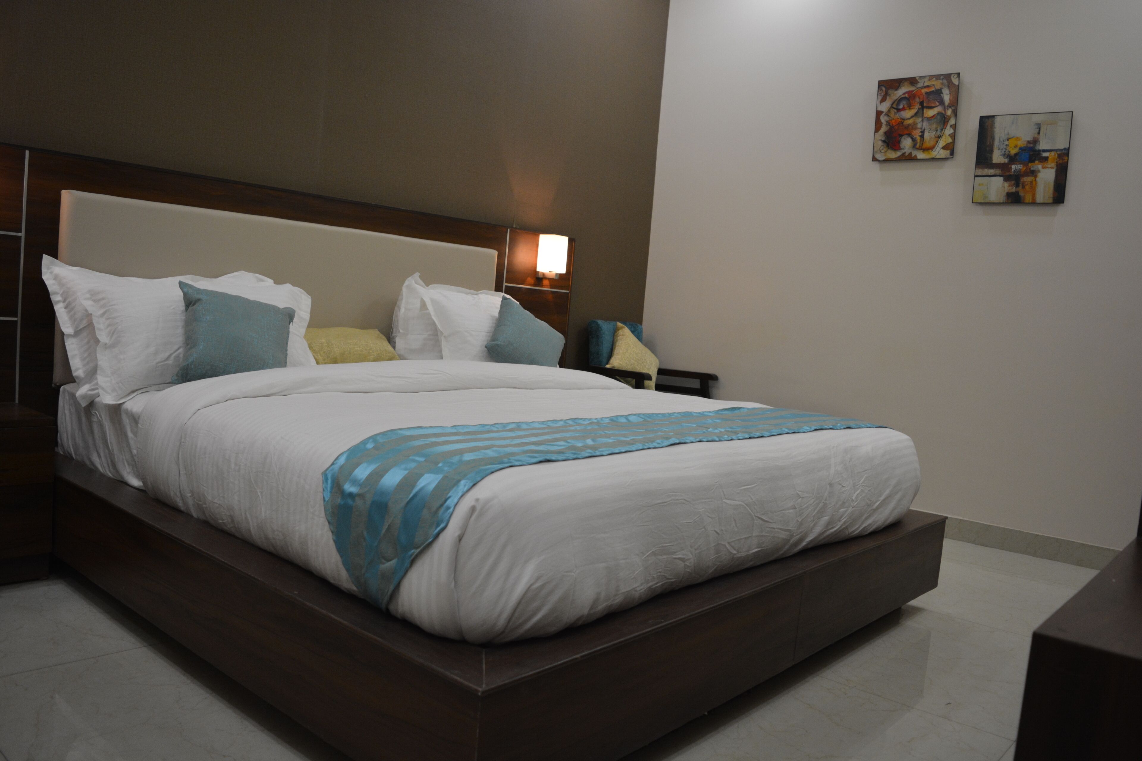 Una habitación de hotel moderna con una cama grande, una mesita de noche y dos cuadros colgados en la pared.