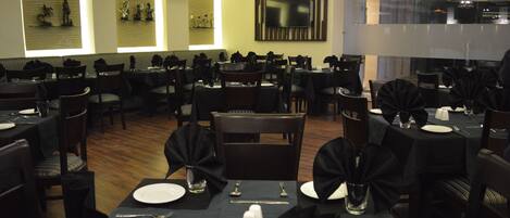 A dining area with multiple tables set for service, a large flat-screen TV mounted on the wall, and a patterned wall decoration.