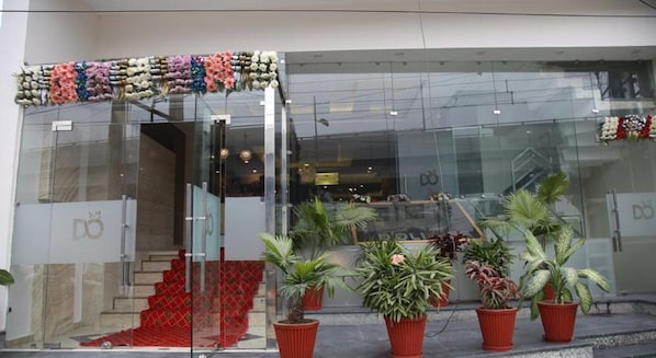 A modern building with a glass facade, red carpeted entrance, and potted plants in front. - Hotel Dolives (Panipat)