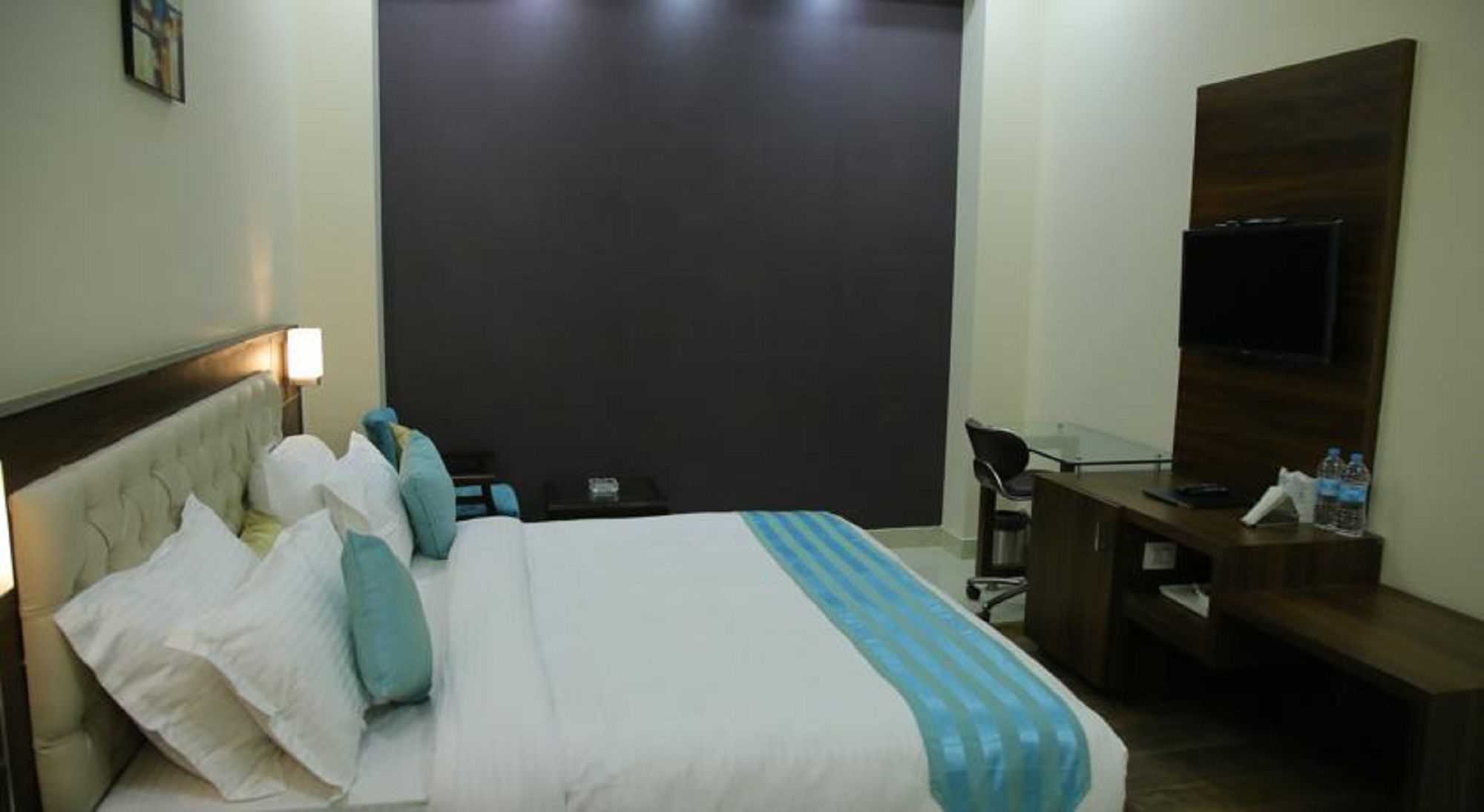 A hotel room with a bed, a desk, a chair, a TV, and a nightstand.