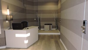 Ein Empfangsschalter mit einem Laptop, einem Telefon und einer Lampe. Zwei Mülleimer und eine Tür mit Schlüsselschloss sind ebenfalls vorhanden.