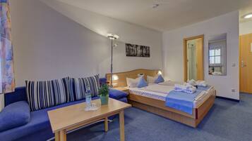 A hotel room with a bed, a sofa, a table, and a lamp.