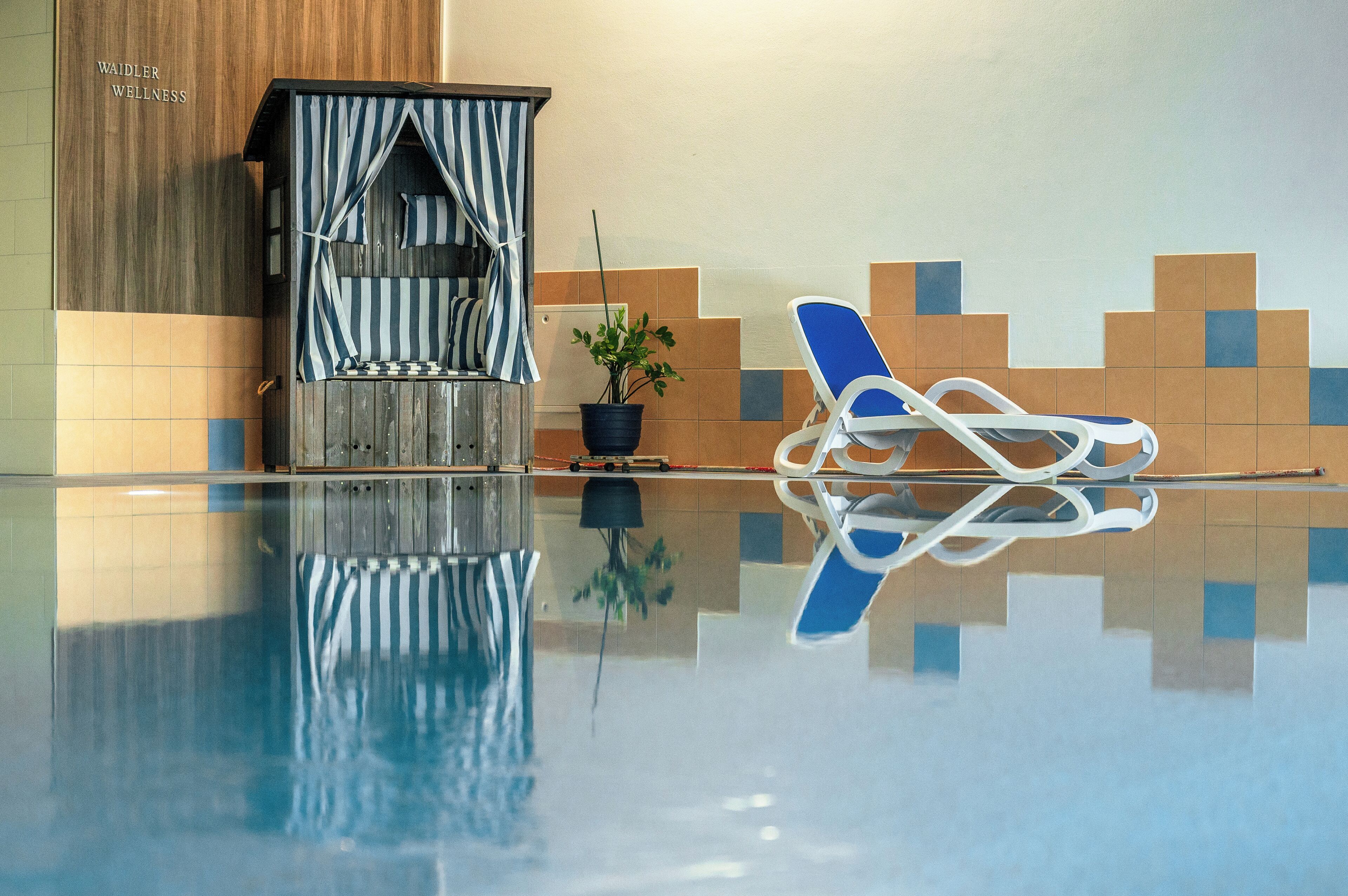 Una piscina nítida amb una cadira de relax i una petita construcció que sembla una casa, amb un teulat a ratlles.