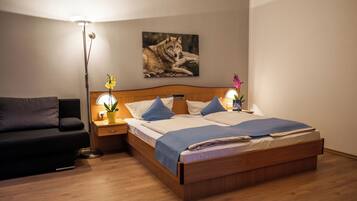 A neatly arranged bedroom with a wooden bed, a nightstand with a lamp, a wall-mounted picture of a wolf, and a potted plant.
