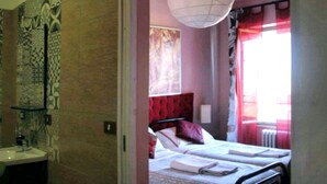 Ein Schlafzimmer mit Bett, Nachttisch, einem Fenster mit Vorhängen sowie einem Badezimmer mit Waschbecken und Spiegel.