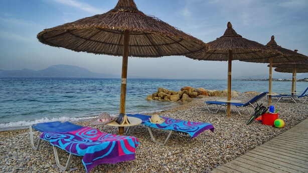 Una playa con sombrillas de paja, sillas de descanso y una orilla de guijarros.
