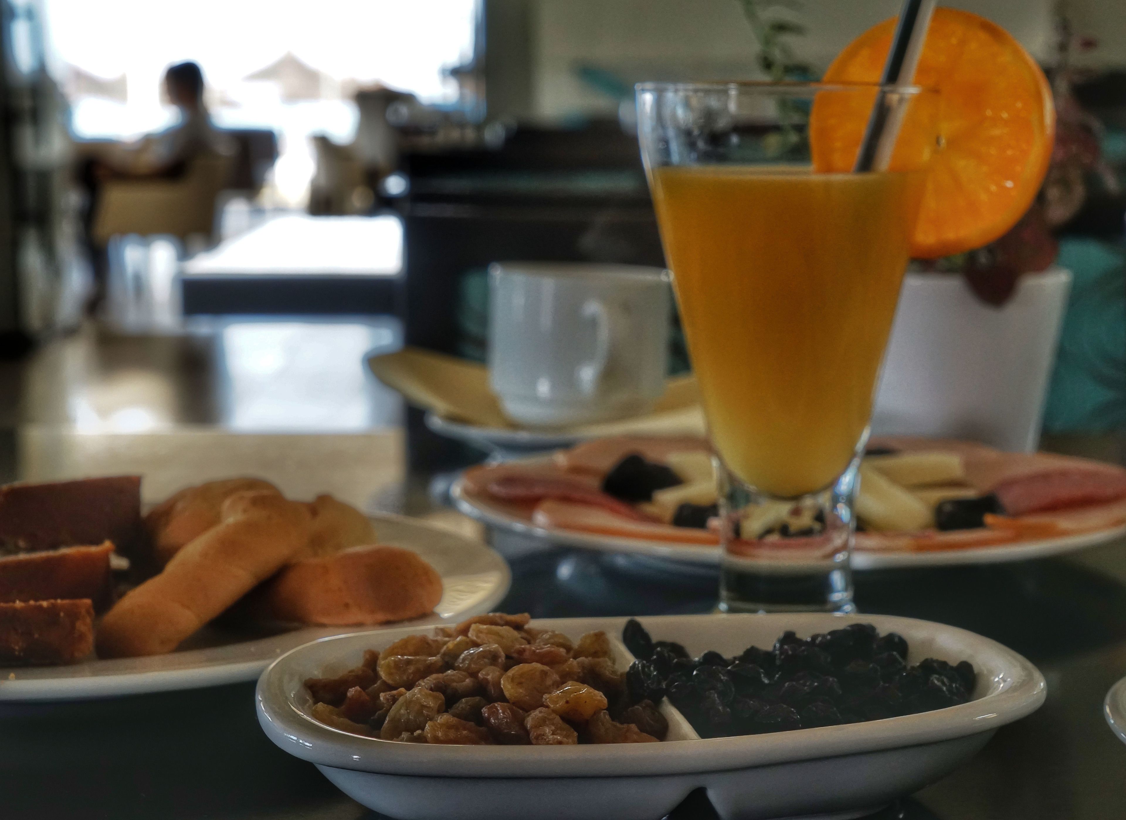 Une table mise pour le petit-déjeuner avec un verre de jus d’orange, une assiette de pain et un bol de fruits secs et de noix mélangés.