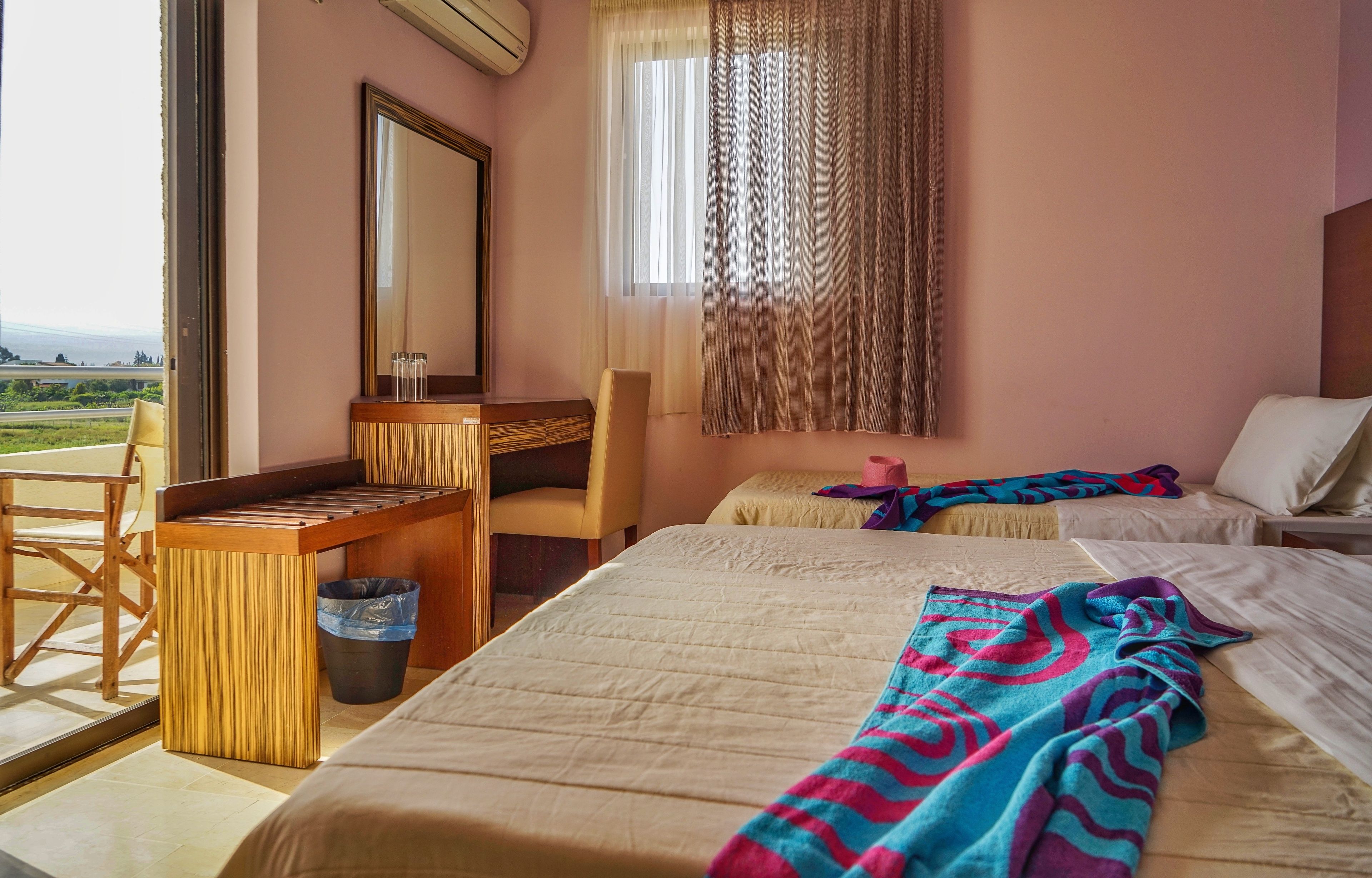 Una camera d'albergo con un letto, una scrivania, una sedia, una finestra con tende e vista sull'esterno.