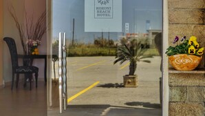 Entrada de un hotel con un letrero del Hotel Kokoni Beach, un estacionamiento y una planta en maceta.