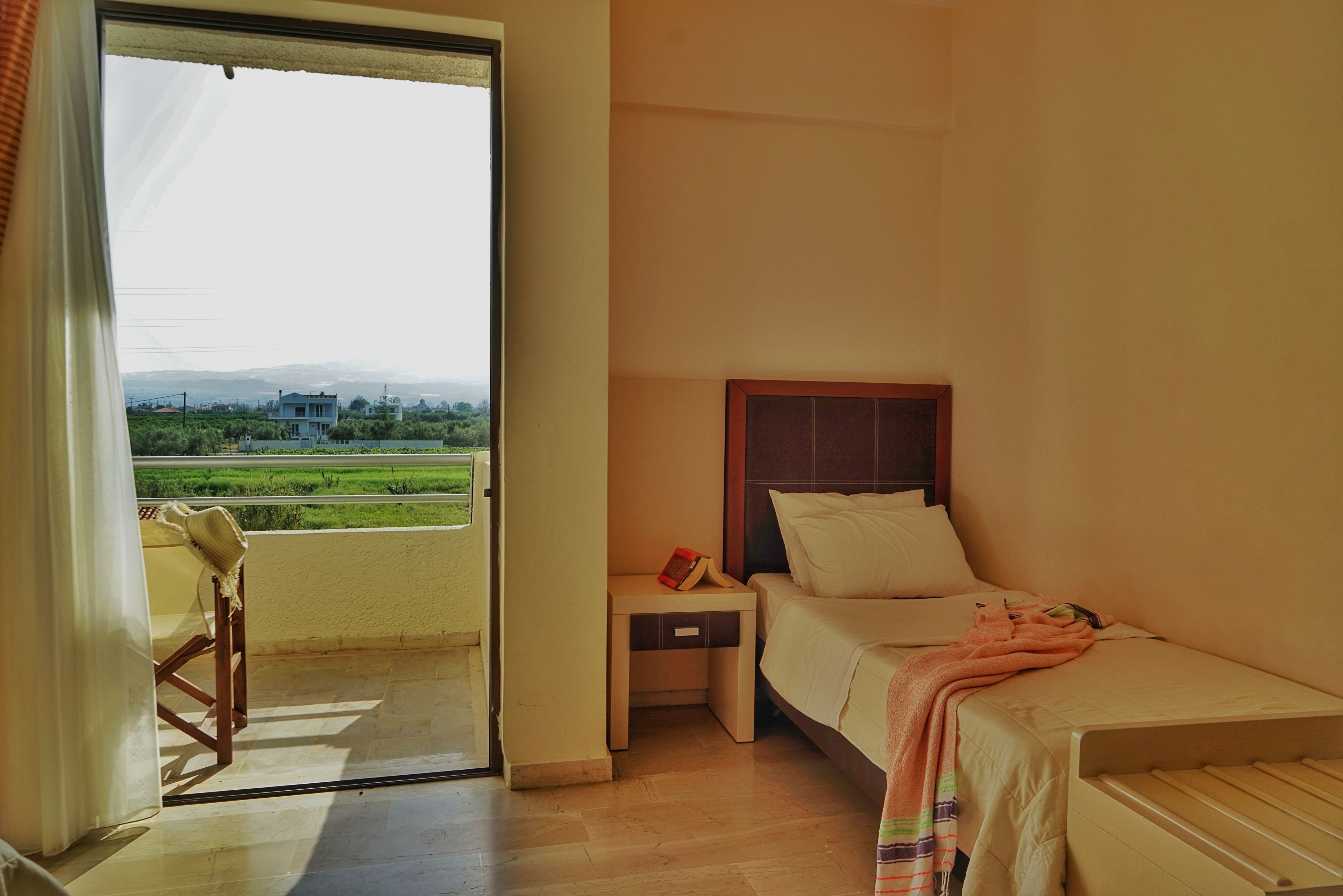 Ein Hotelzimmer mit Bett, Nachttisch, Stuhl und Blick auf eine grüne Landschaft durch eine offene Tür.