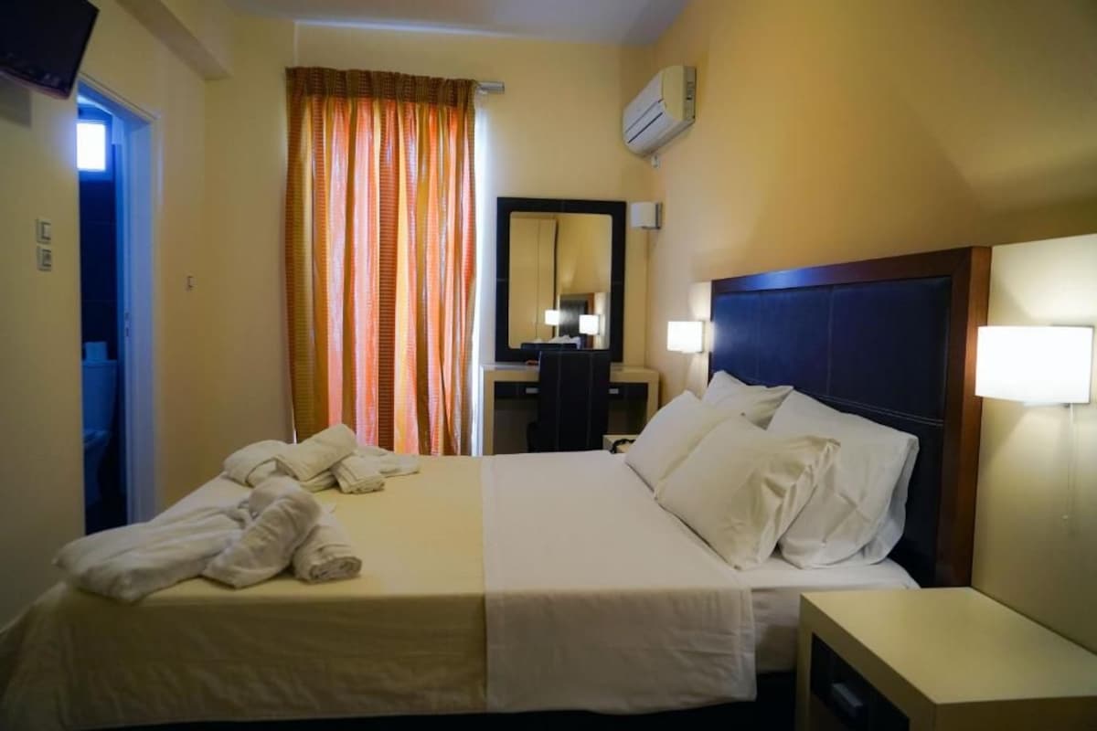 A hotel room with a bed, a bedside table, a mirror, and a window with curtains.