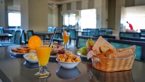 Una mesa de desayuno con jugo de naranja, un tazón de cereal y una canasta de pan.