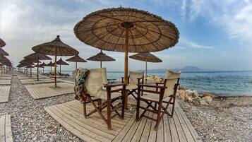 A wooden deck with thatched umbrellas and chairs by the sea.