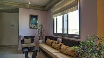 A living room with a sofa, a chair, a small table, a potted plant, and a window with blinds.
