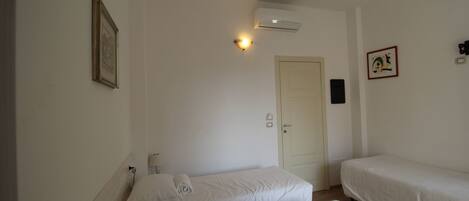 Una habitación con dos camas individuales, una puerta, un equipo de aire acondicionado y una lámpara fijada a la pared.