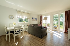 A spacious living area with a sofa, dining table, chairs, and a large window. - Haus Ostseeblick (Göhren)