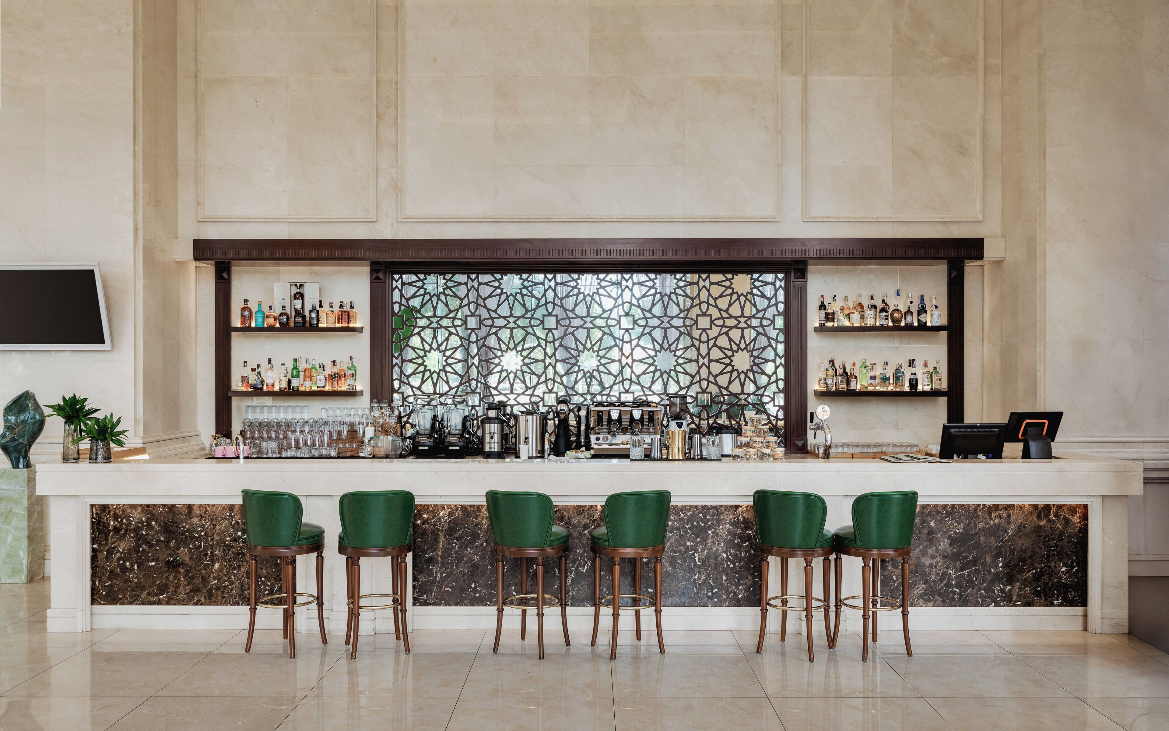 A bar area with a marble countertop, green bar stools, and shelves stocked with bottles.