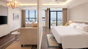 Quarto de hotel com cama grande, televisão, sofá e vista para a cidade.