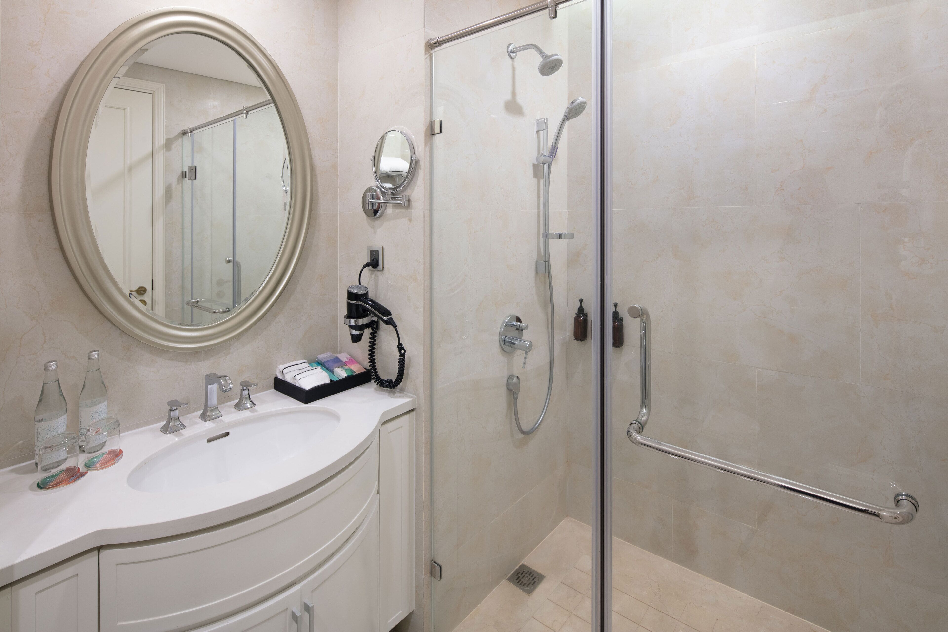 Un baño moderno con cabina de ducha de vidrio, un tocador blanco con espejo redondo y un lavamanos blanco.