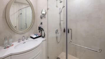 Un baño moderno con cabina de ducha de vidrio, un tocador blanco con espejo redondo y un lavamanos blanco.