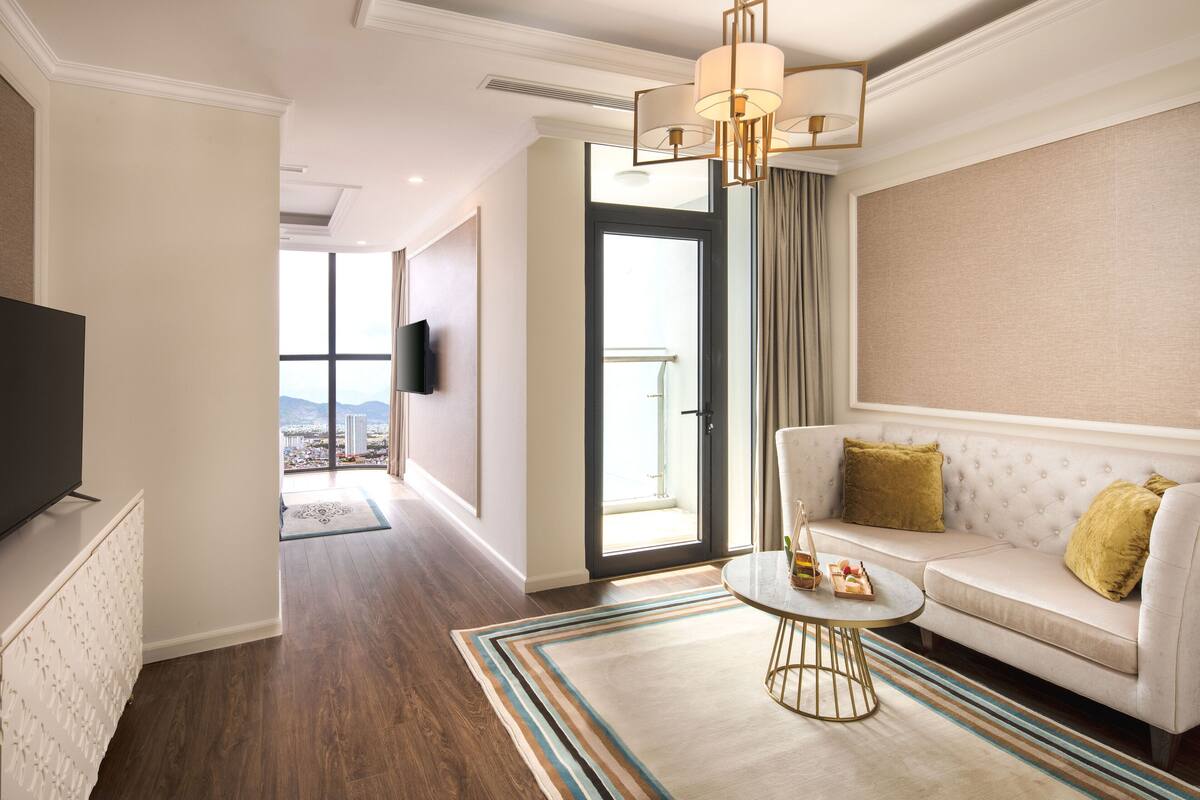 Ein Hotelzimmer mit Sofa, Couchtisch, Fernseher und Blick auf die Stadt durch ein großes Fenster.