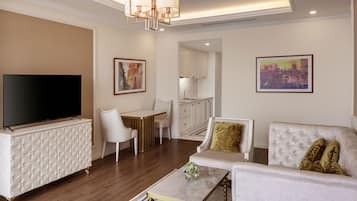 A modern living room with a flat-screen TV, a white sofa, a coffee table, and a dining area with a white table and chairs.