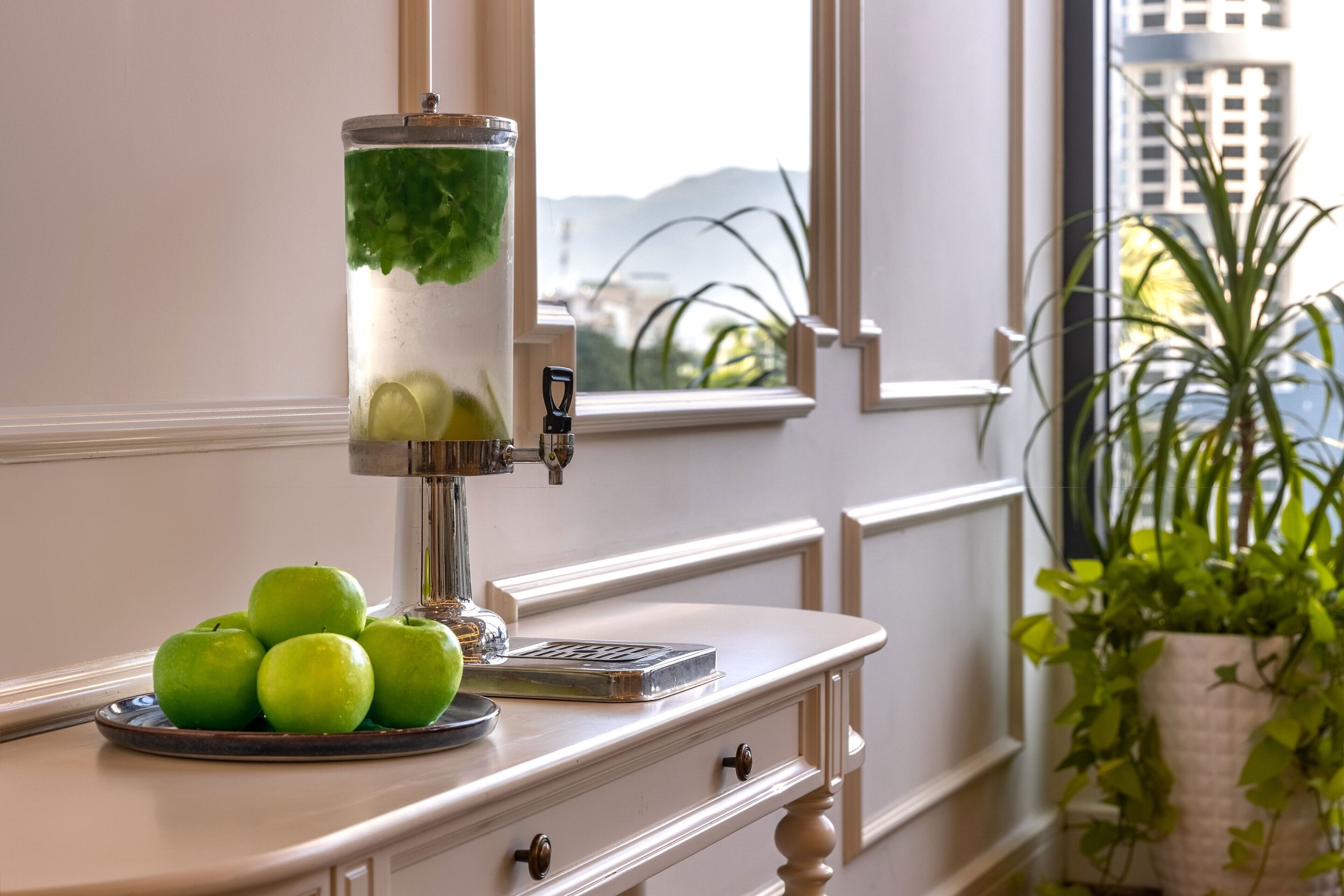 A kitchen counter with a water dispenser, a plate of green apples, and a potted plant.
