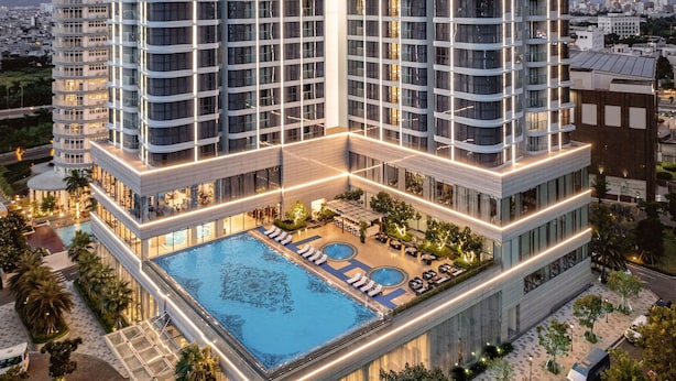 Un hôtel de grande hauteur doté d’une piscine sur le toit, de nombreux balcons et d’une façade bien éclairée.