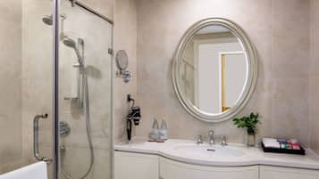 Un baño moderno con ducha envuelta en vidrio, un espejo redondo grande y un tocador blanco con lavamanos y toallero.