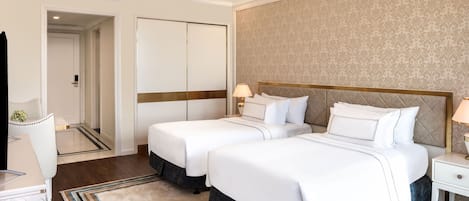 A hotel room with two beds, a desk, a chair, a nightstand, and a ceiling fan.