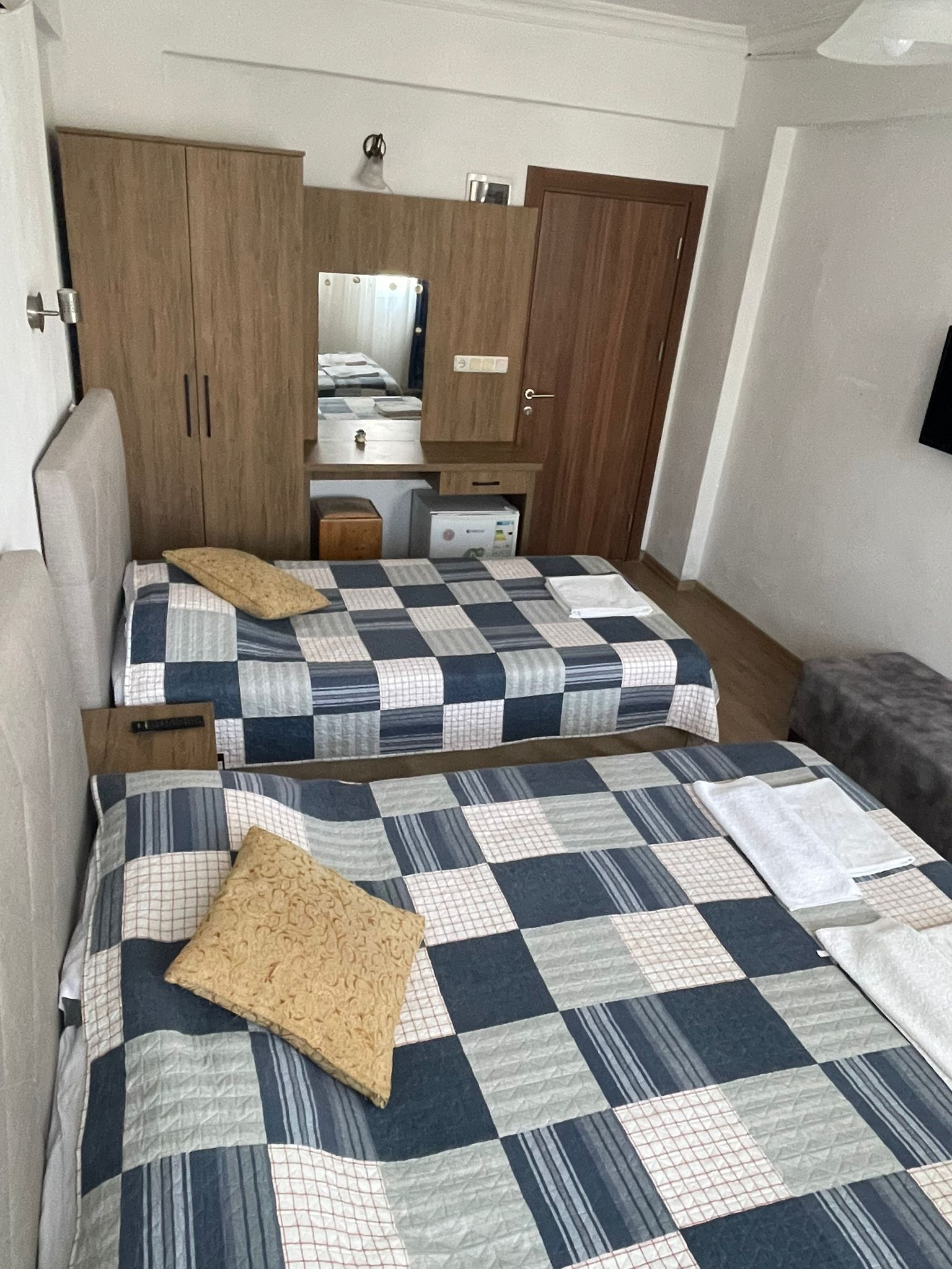 Quarto com duas camas, um guarda-roupa, um espelho e uma pequena cozinha compacta.