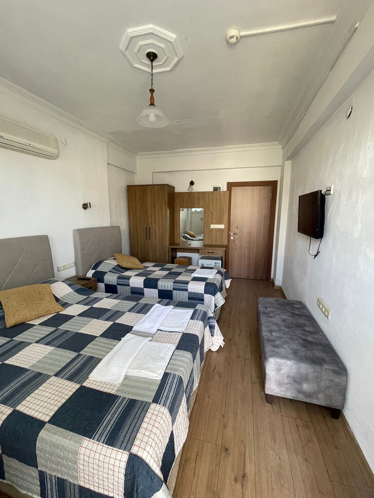 Een slaapkamer met twee bedden, een bankje, een spiegel en een televisie.