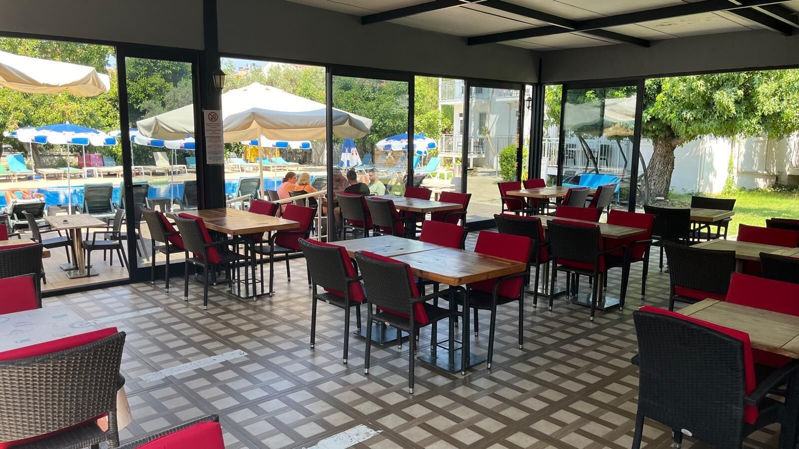 Un área de comedor al aire libre con mesas y sillas, una piscina al fondo y vistas de los alrededores.