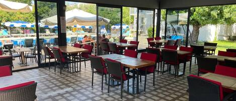 Un área de comedor al aire libre con mesas y sillas, una piscina al fondo y vistas de los alrededores.