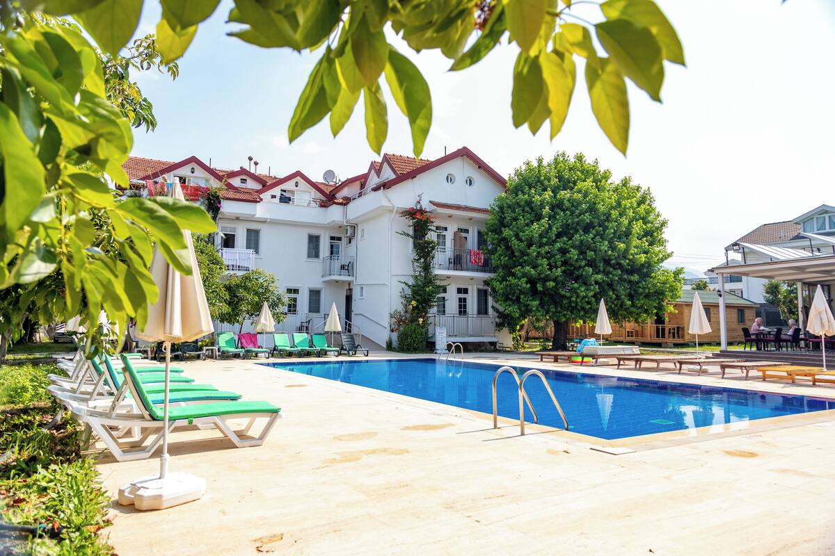 A swimming pool with lounge chairs and umbrellas, surrounded by a building with a red roof and balconies.