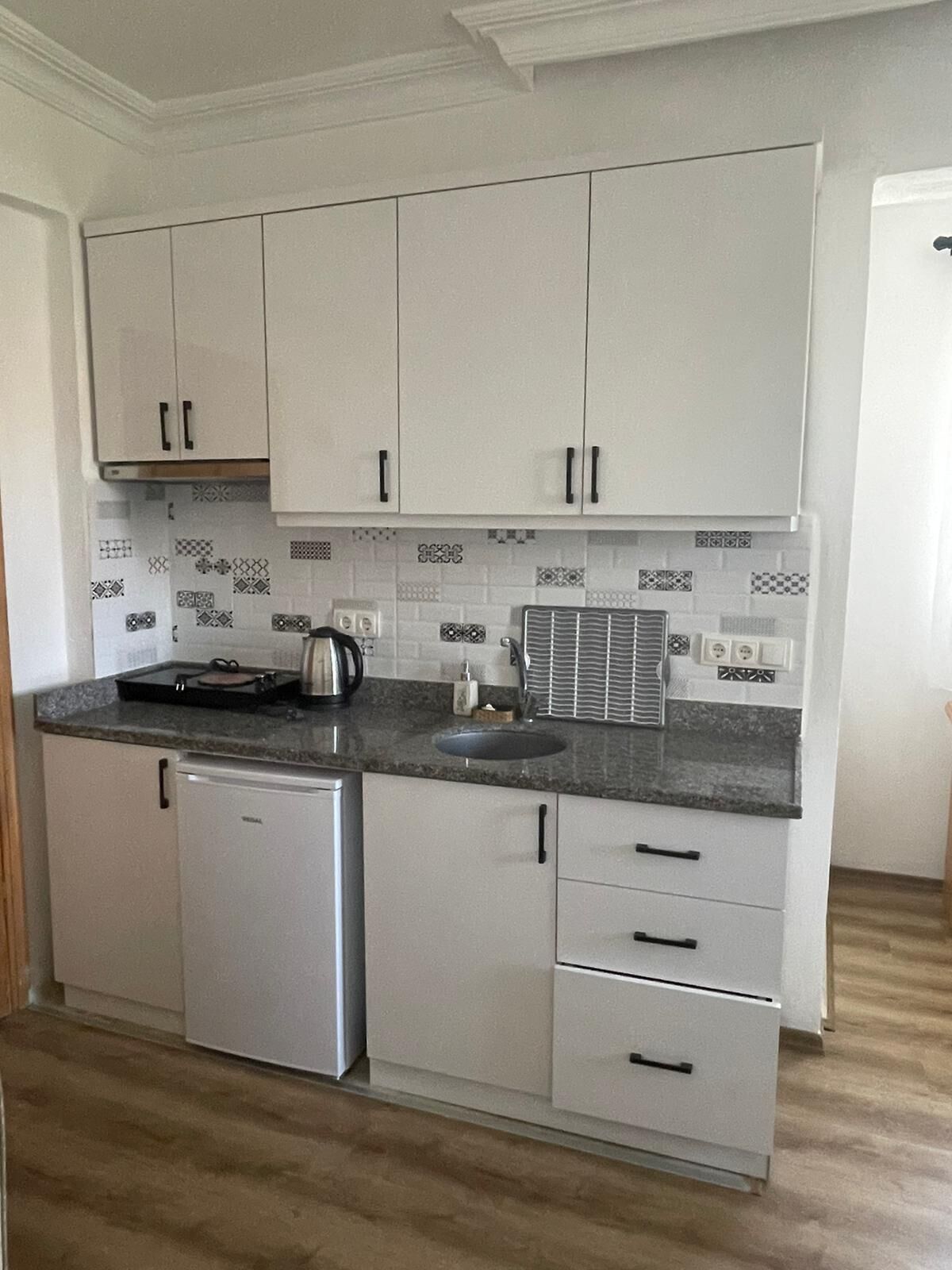 A compact kitchen with white cabinets, a built-in dishwasher, a sink, and a patterned backsplash.