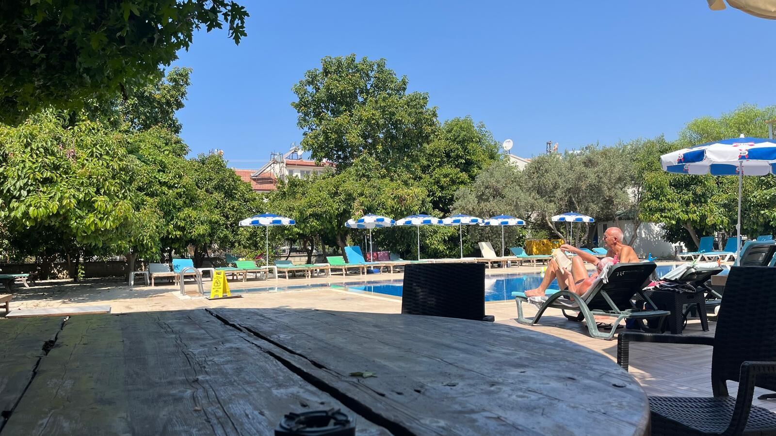 A poolside area with lounge chairs, umbrellas, and a wooden table.