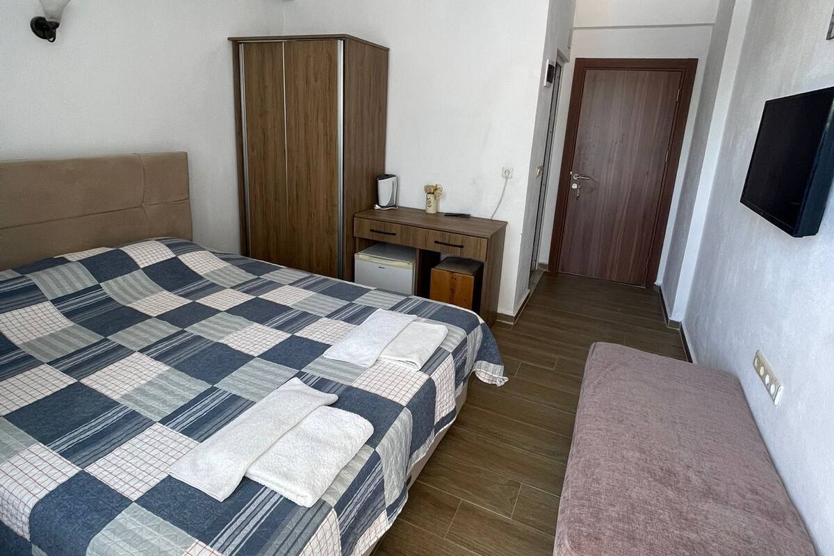 A bedroom with a bed, a desk, a wardrobe, a television, and a bench.