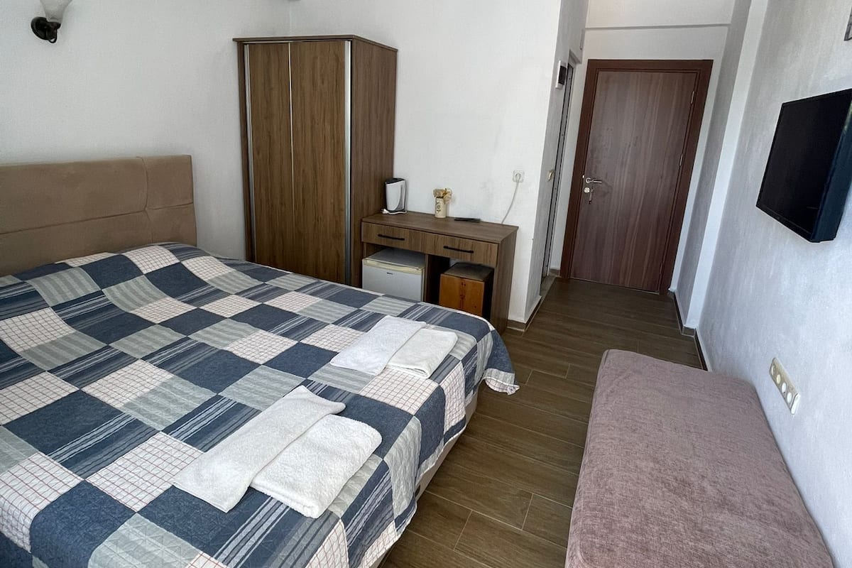 Un dormitorio con cama, escritorio, armario, televisor y un banco.